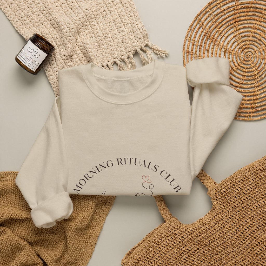Morning Rituals Club crewneck folded flat with a candle, woven placemat, and knit throw