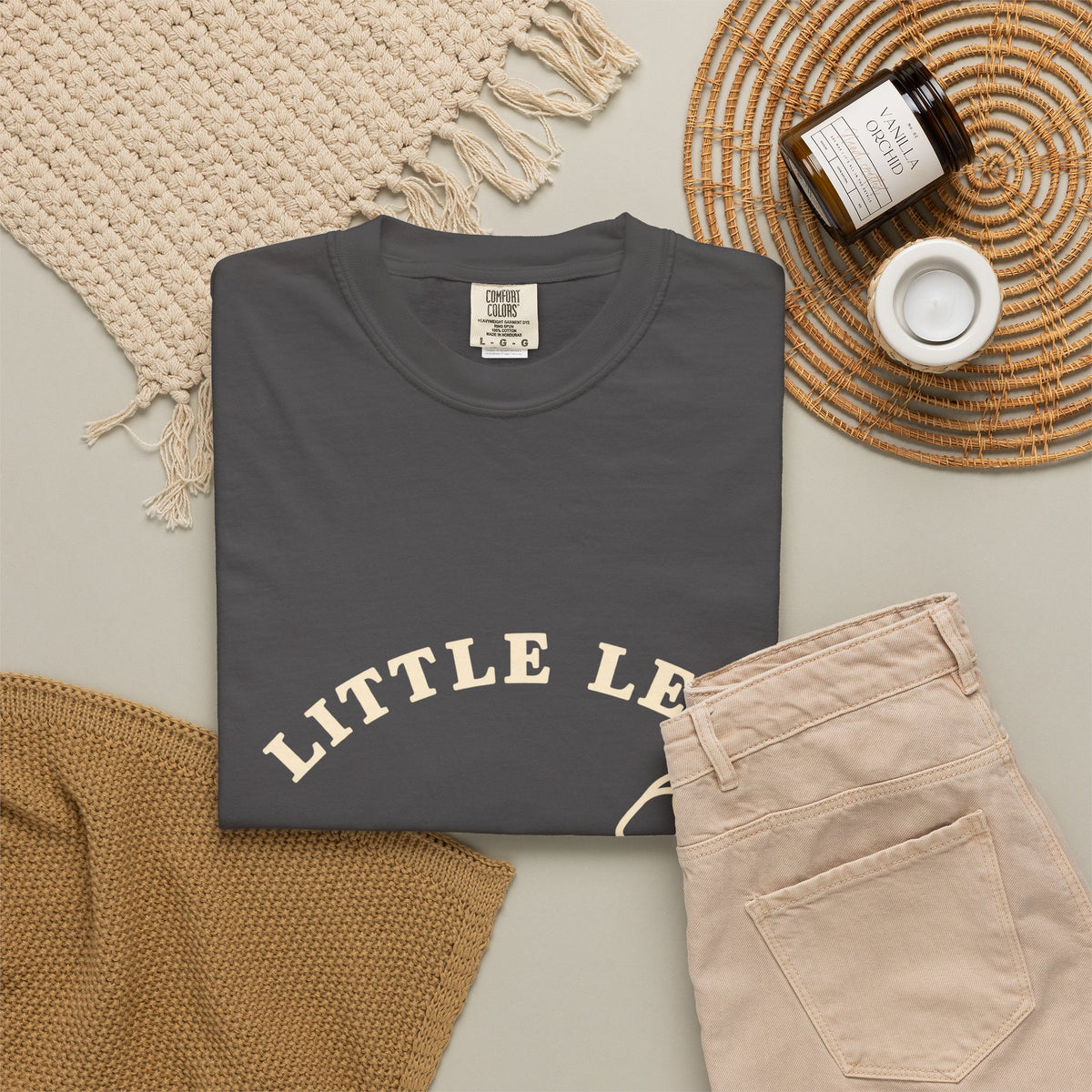 Little Legs Big Heart tee folded flat with a candle, jeans, and a woven placemat