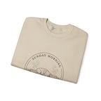 Close-up of the Sunday Morning Sofa Club badge on a folded sand crewneck