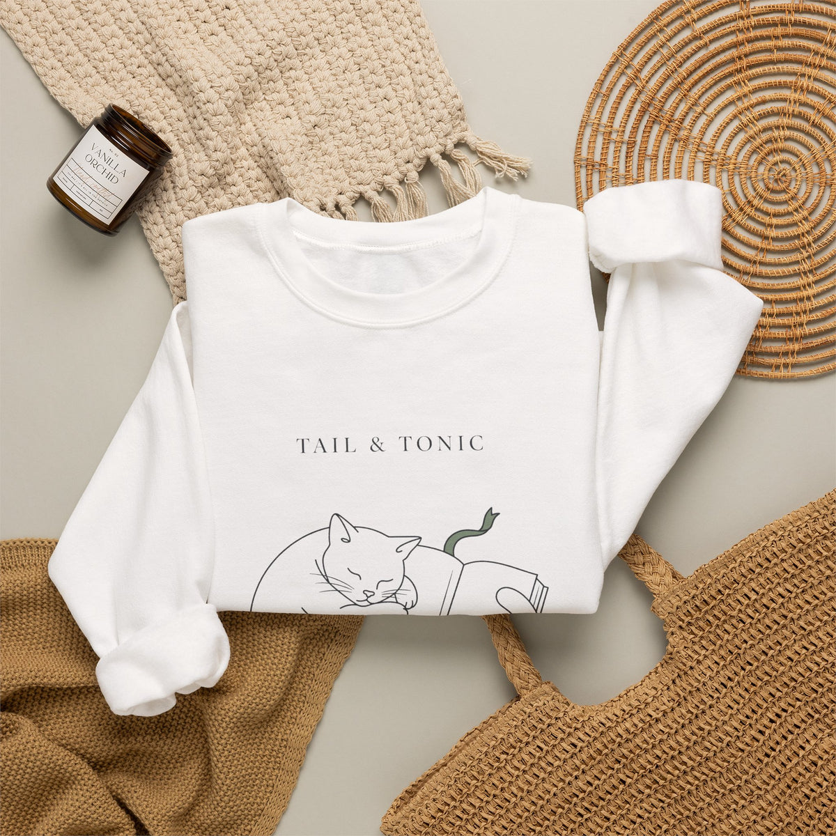 White Quiet Company crewneck folded flat with a candle, woven placemat, and knit throw
