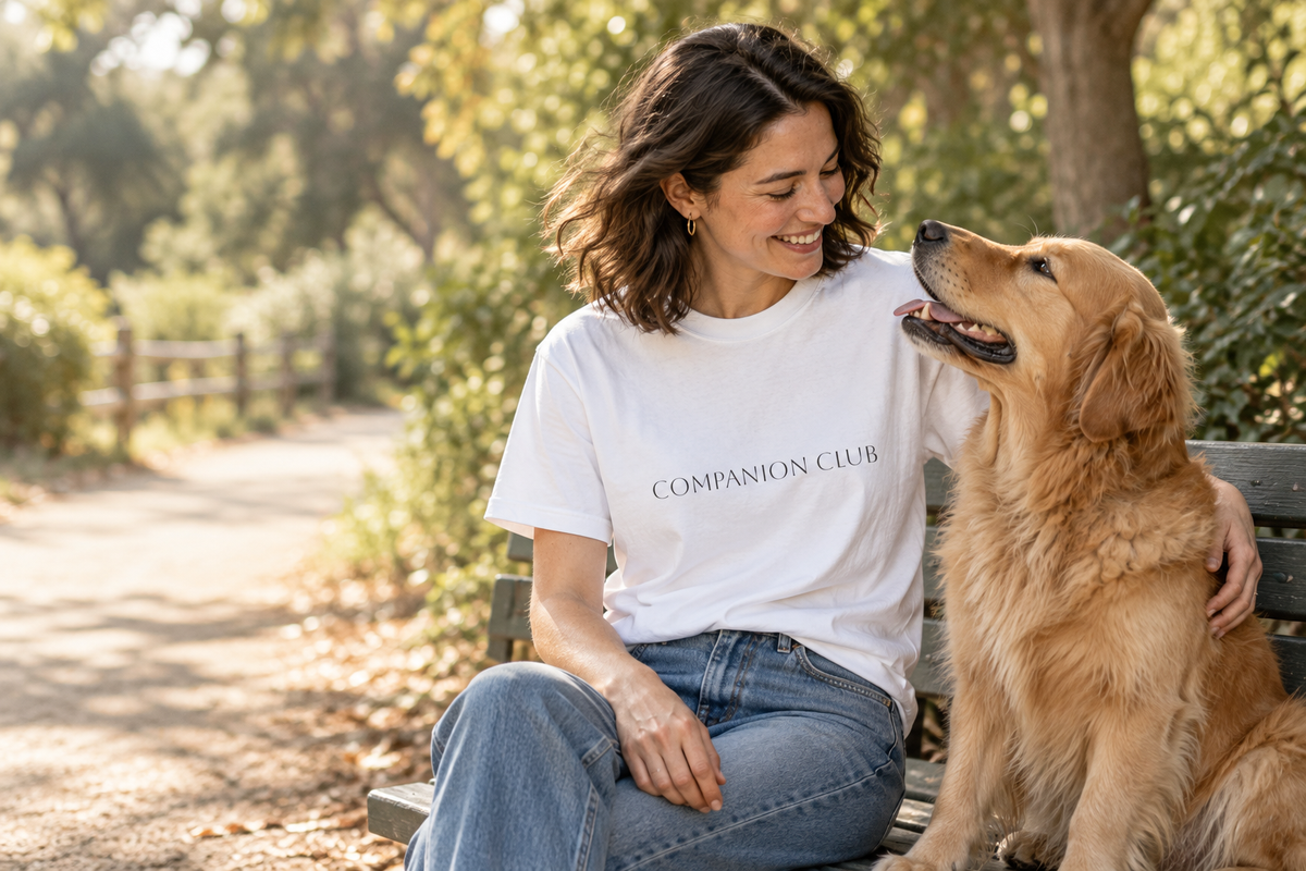 Lifestyle model mockup: woman wearing the white Companion Club tee with a golden retriever.